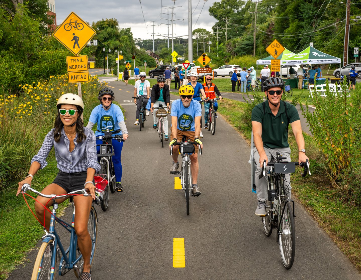 Group of cyclists on a sunny trail, wearing helmets, surrounded by greenery.