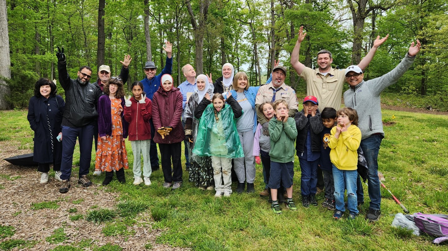 Group of people smiling and raising arms in a wooded park setting.