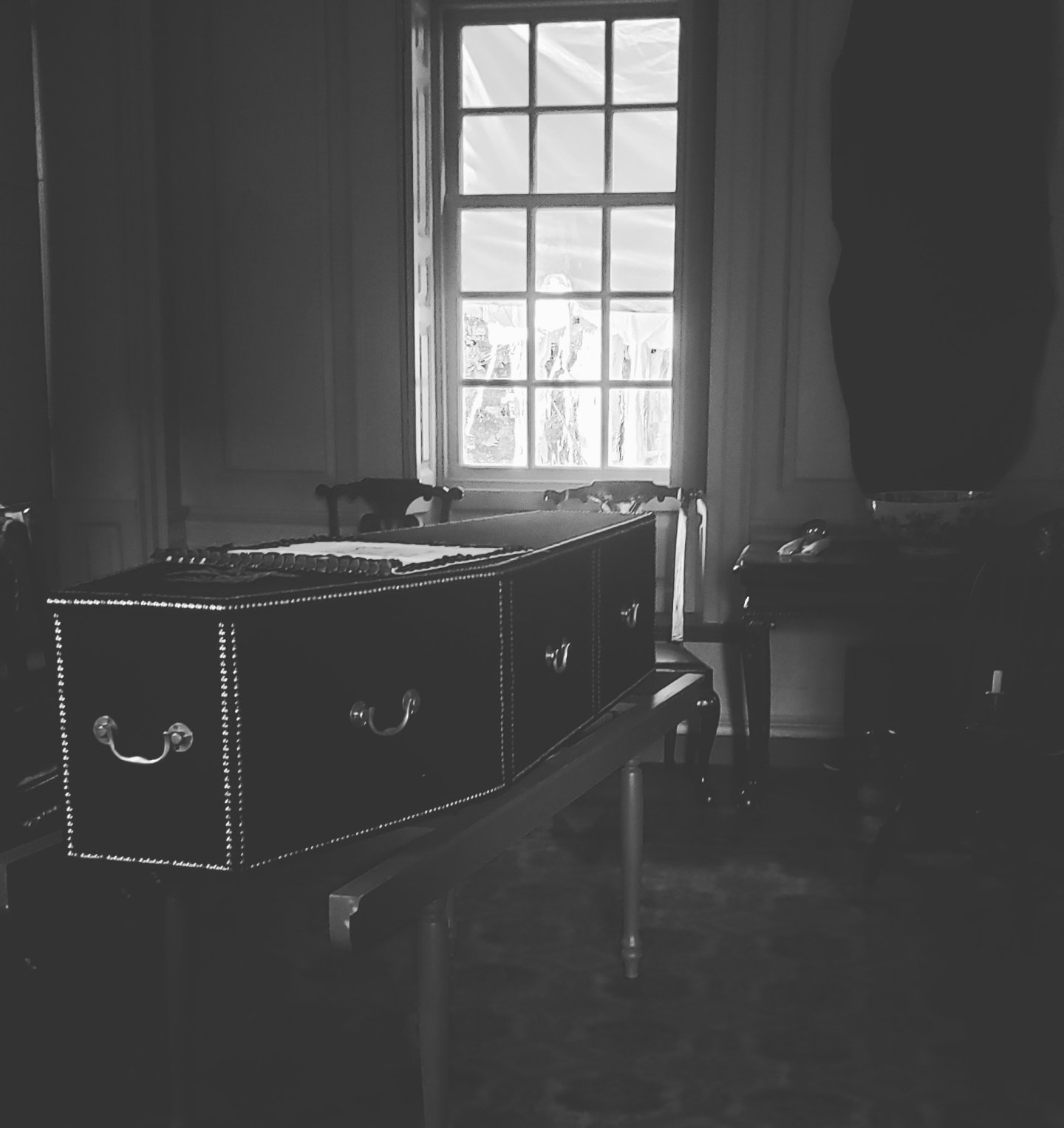 A black and white photo of a vintage room with a chest and window.