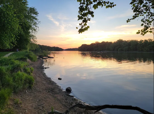Sunset over a calm river with trees lining the bank.