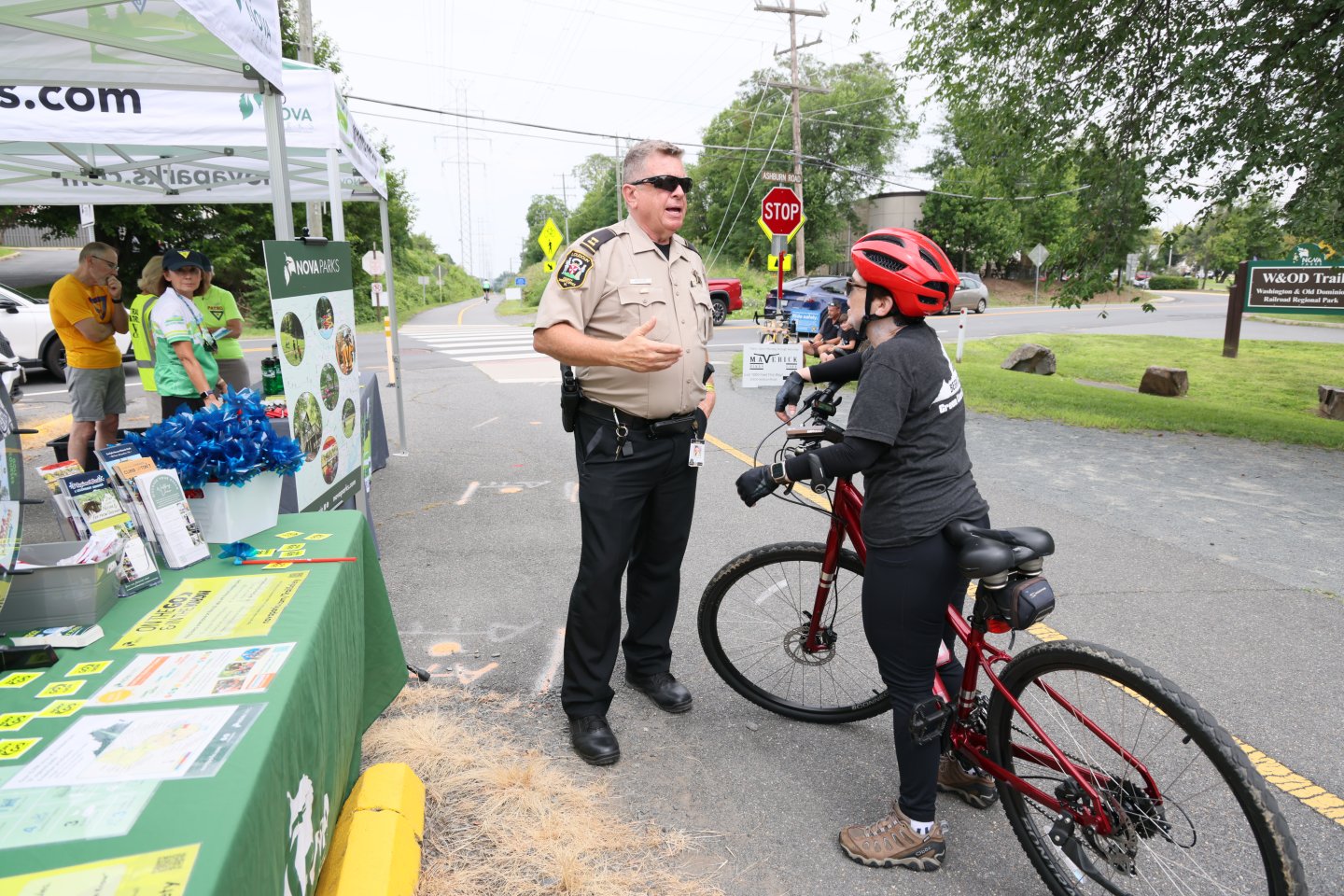 Police officer speaking with a cyclist beside a road at a community event.